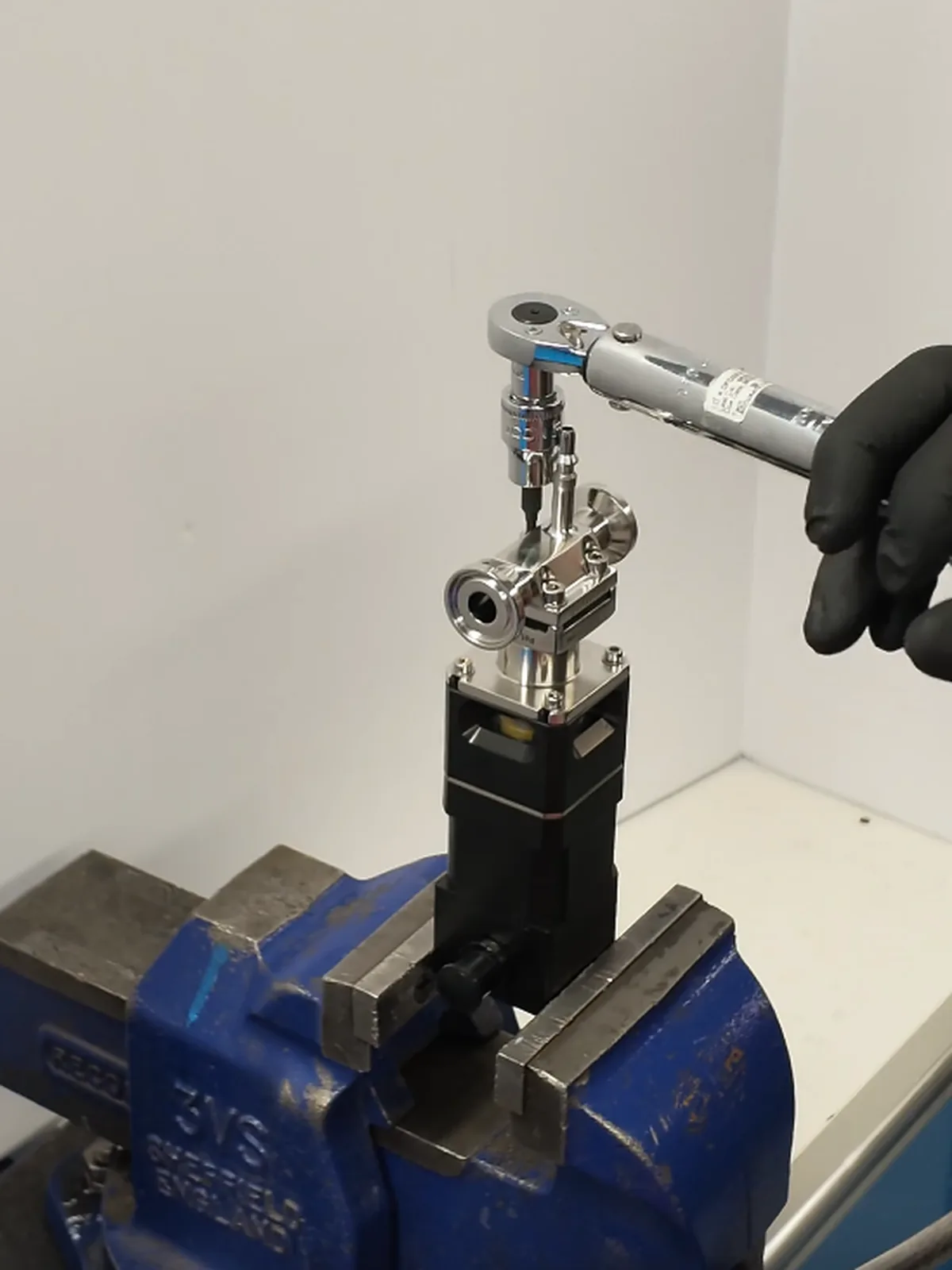 A stainless diaphragm valve on its actuator, held in a bench vise while a torque wrench is applied