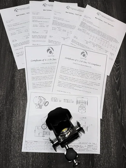 A valve resting on its documentation pack: material test reports and USP Class VI certificates fanned out around it